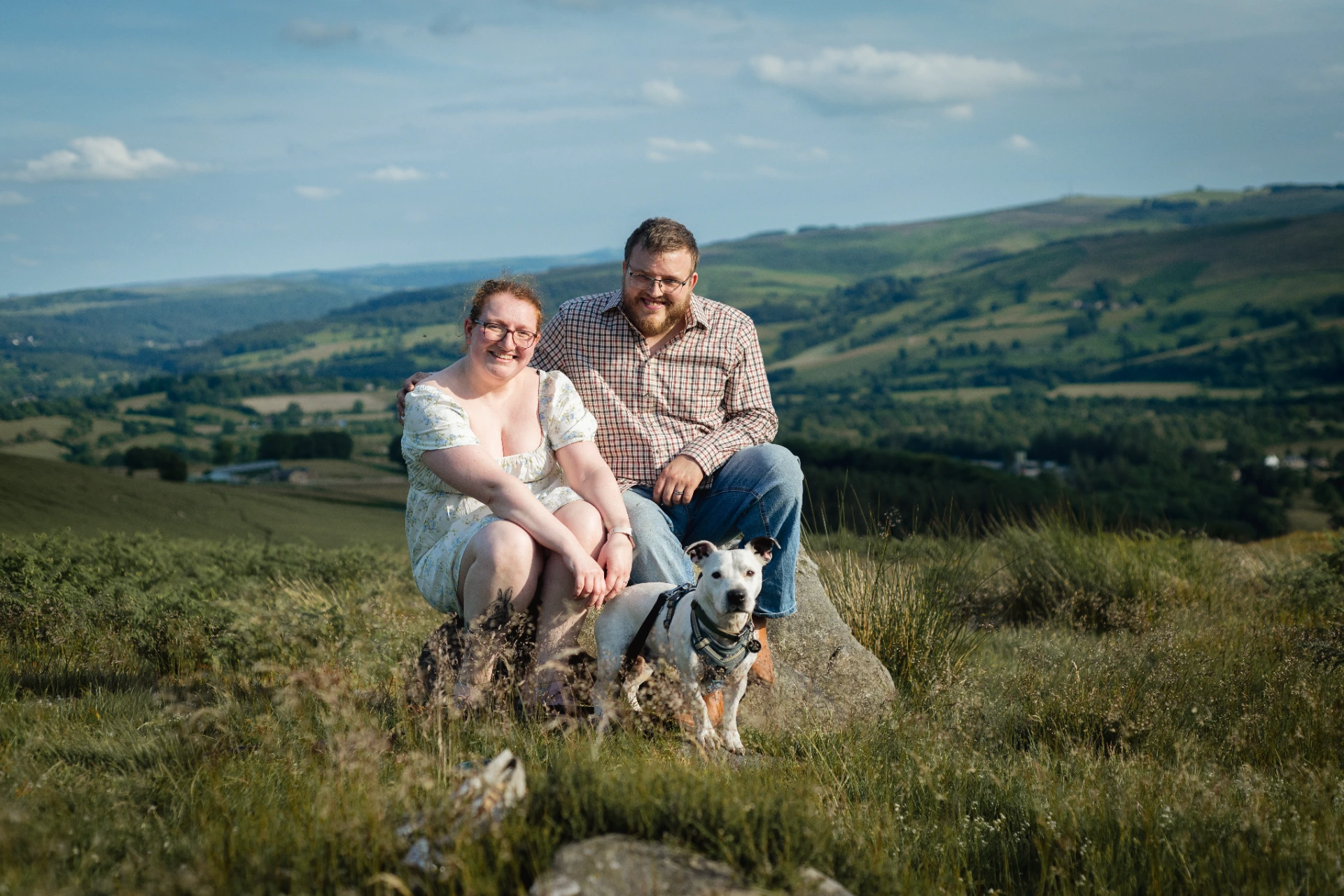 A couple sitting on a rock with their dog overlooking the countryside