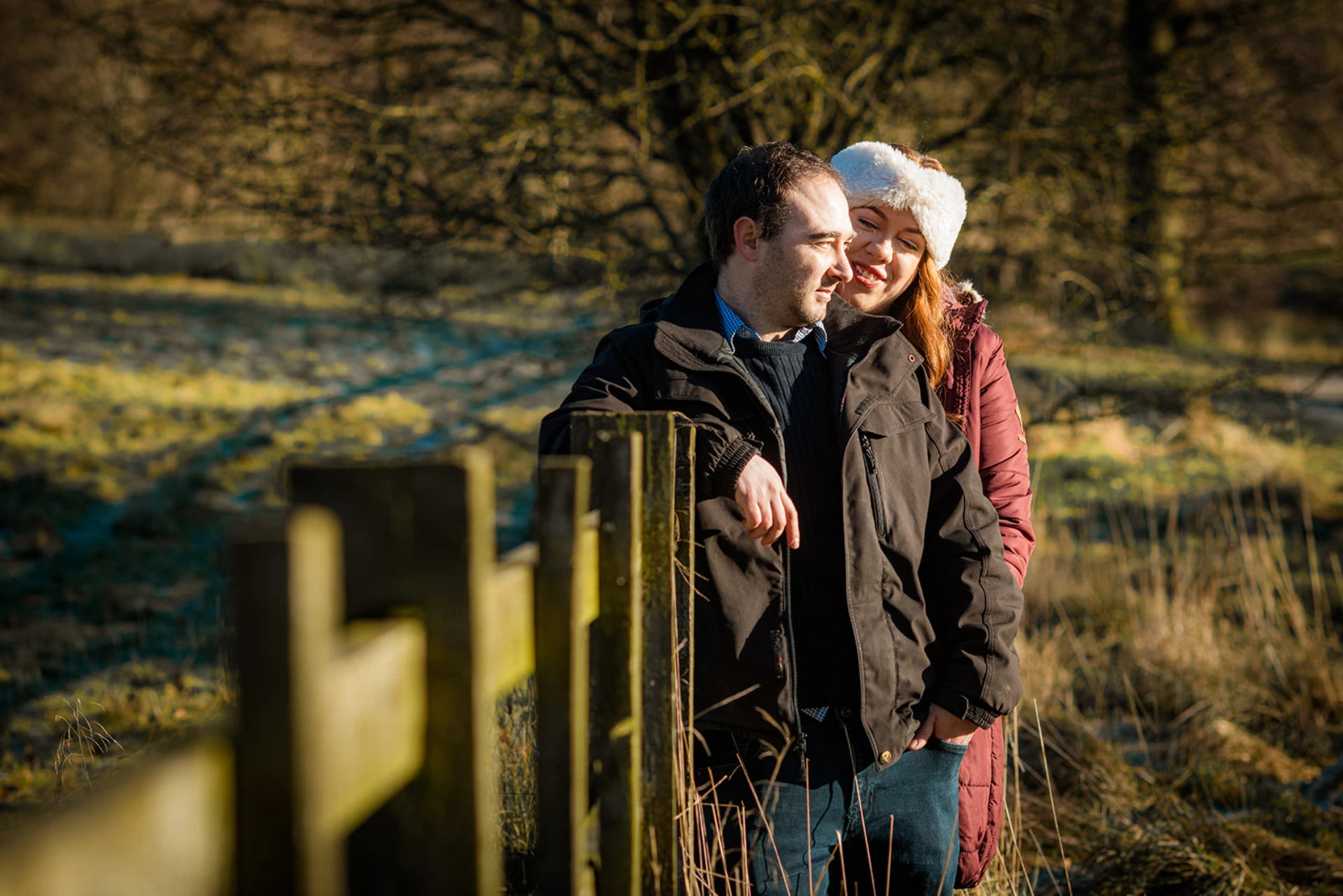 A couple standing by a wooden gate in warm evening light